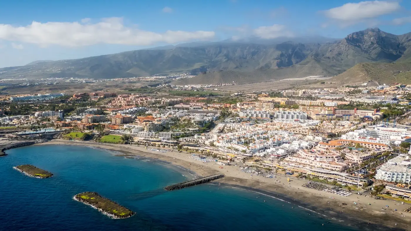 A stunning aerial shot of a coastal town in Tenerife, Canary Islands with mountains in the background.