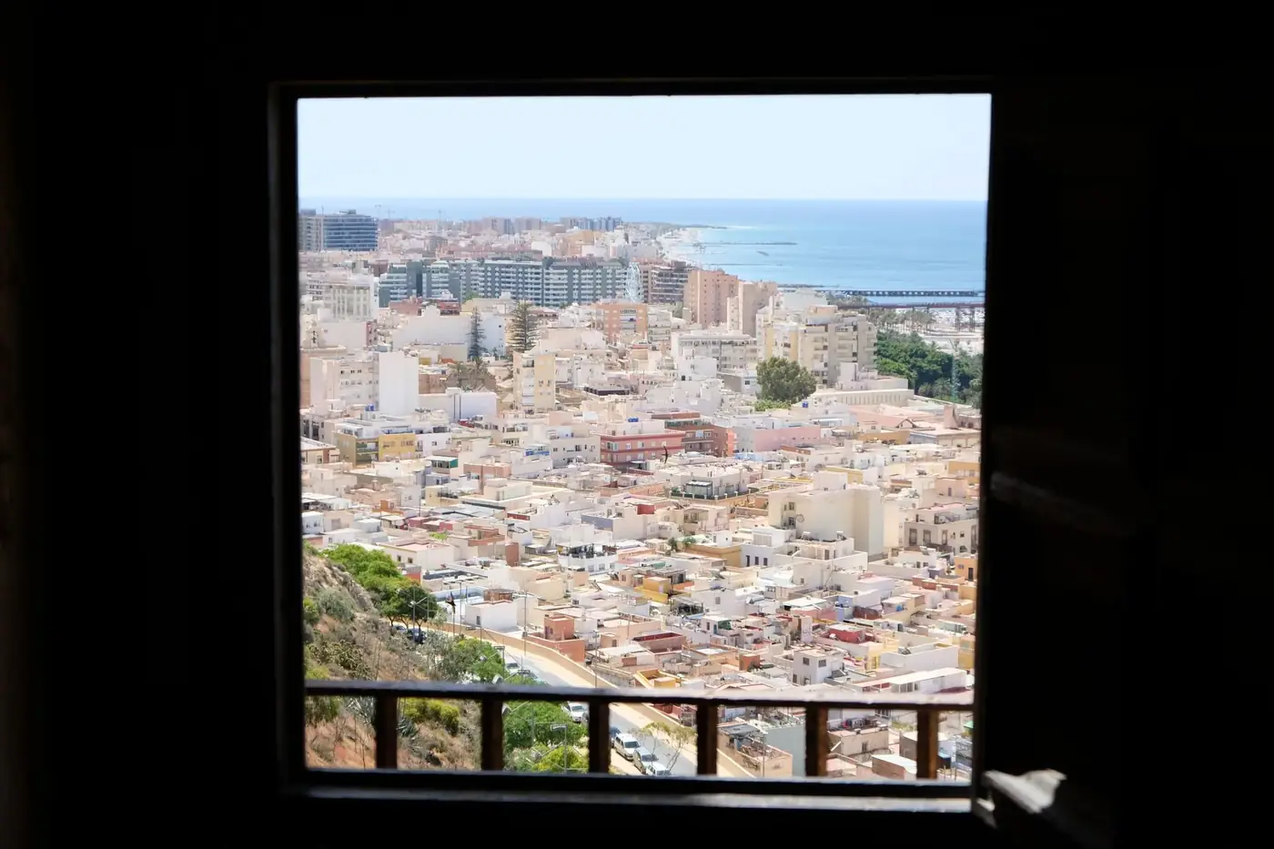Aerial view of an urban coastal city through a window frame, showcasing buildings and the sea.