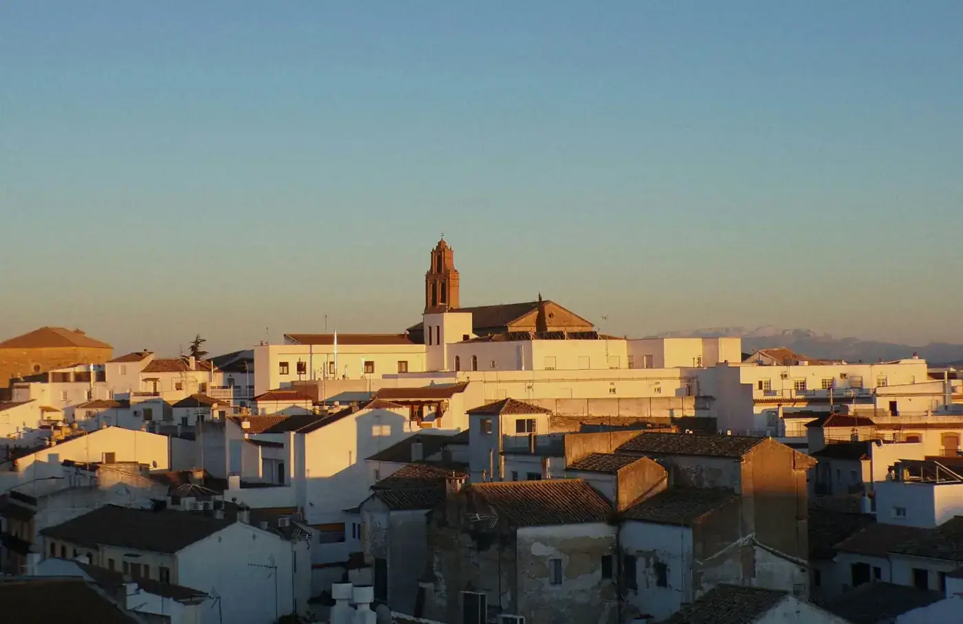 A picturesque view of a Spanish village with white buildings at sunset, highlighting a church tower and distant mountain