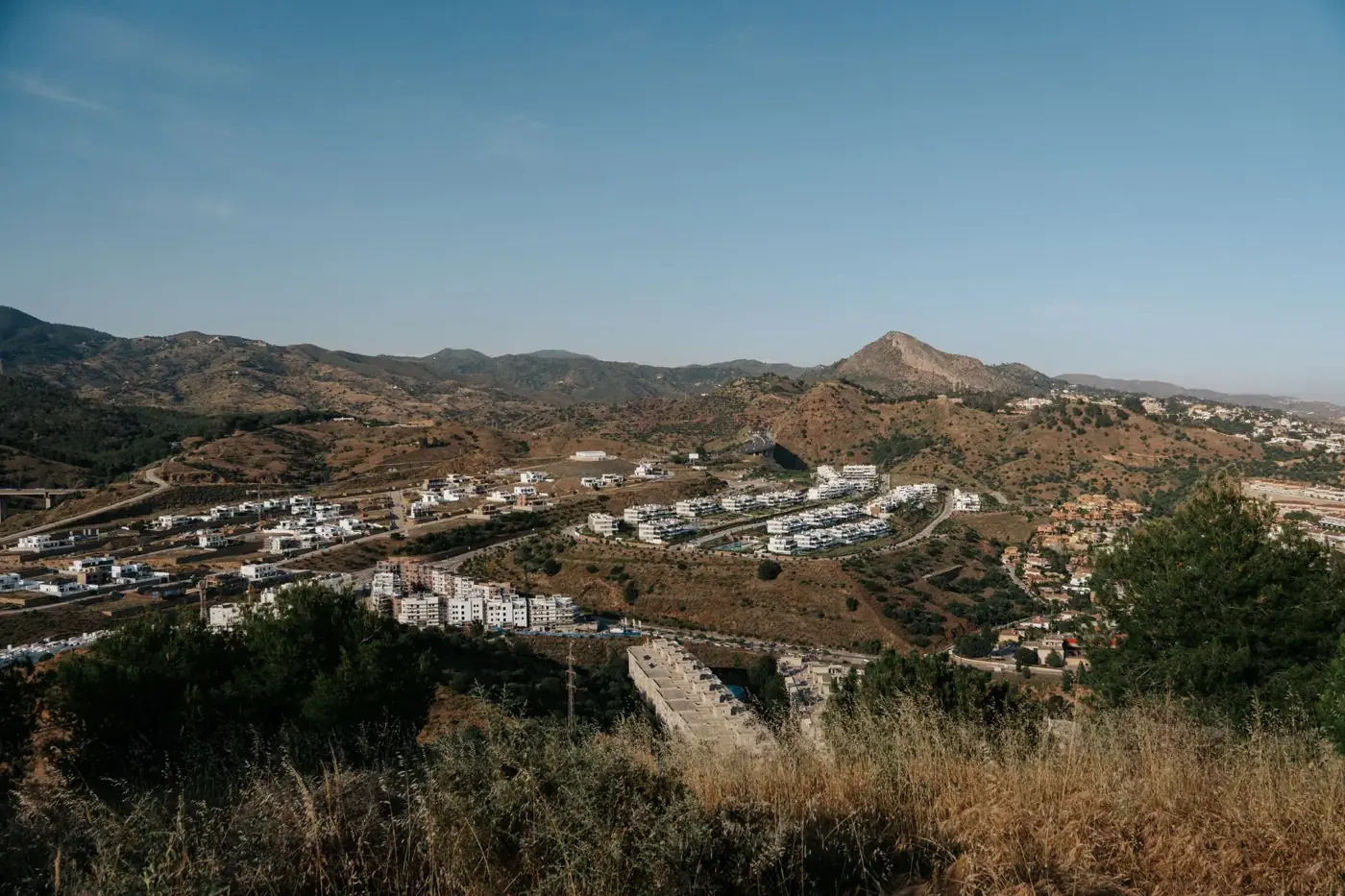 Capture of Málaga, Spain's scenic landscape featuring white buildings nestled in rolling hills under a clear summer sky.