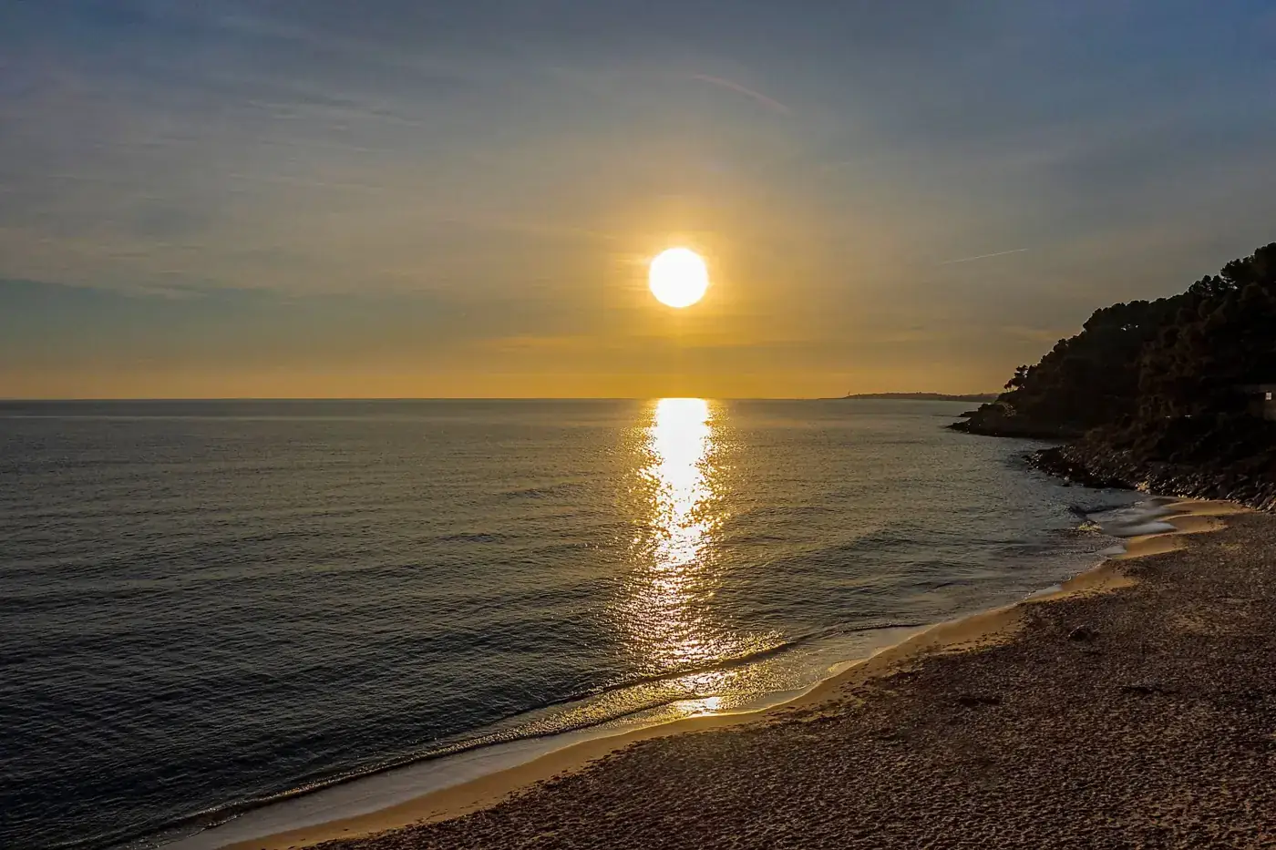 Sunset casts golden hues over a peaceful Catalonia beach, capturing serene coastal beauty.