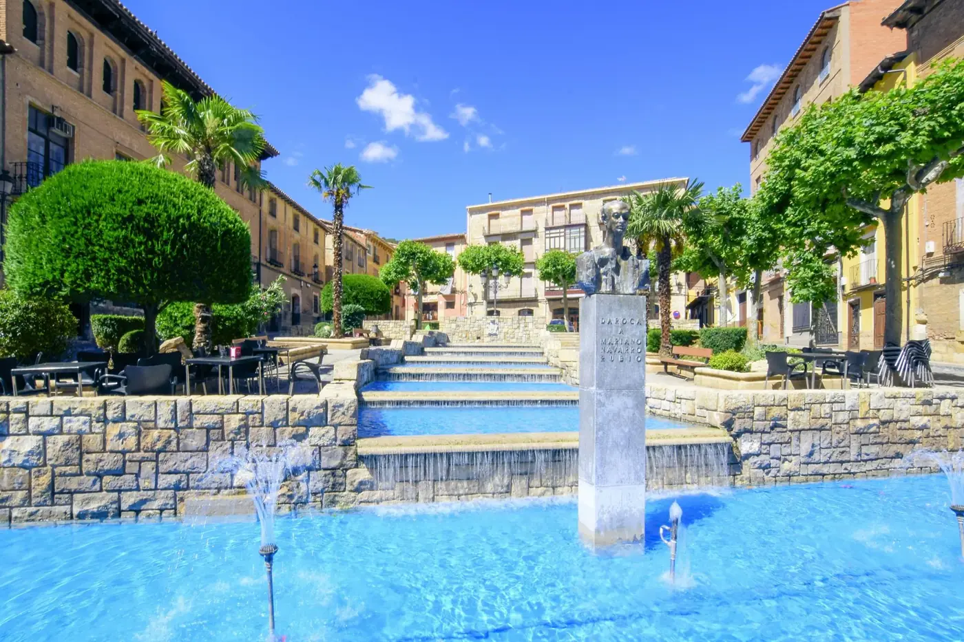 Beautiful stone fountain and statue in Daroca, Spain with vibrant blue water and lush greenery.