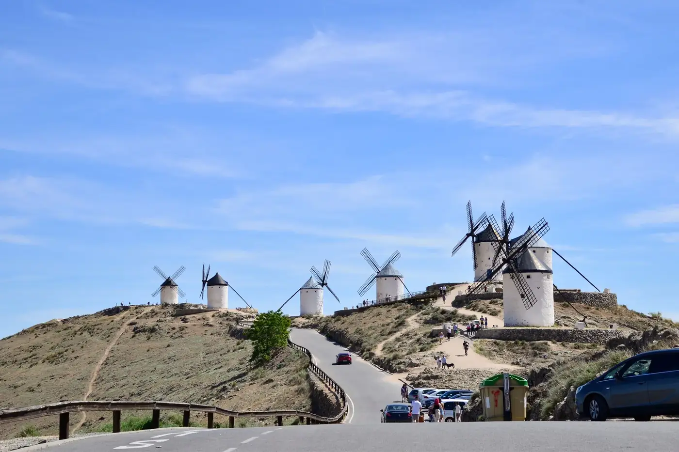 Scenic view of historic windmills on a hill in Consuegra, Spain, under a bright blue sky.
