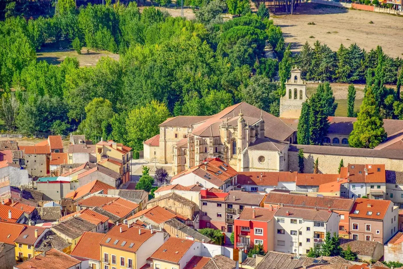 Scenic view of Peñafiel, Spain featuring a historic monastery surrounded by vibrant rooftops and lush greenery.