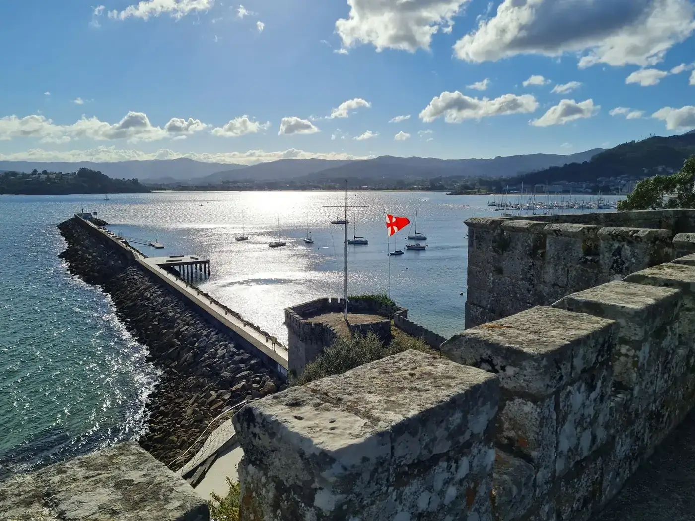 A stunning coastal view featuring a historic fortress and sailboats on a sunny day.