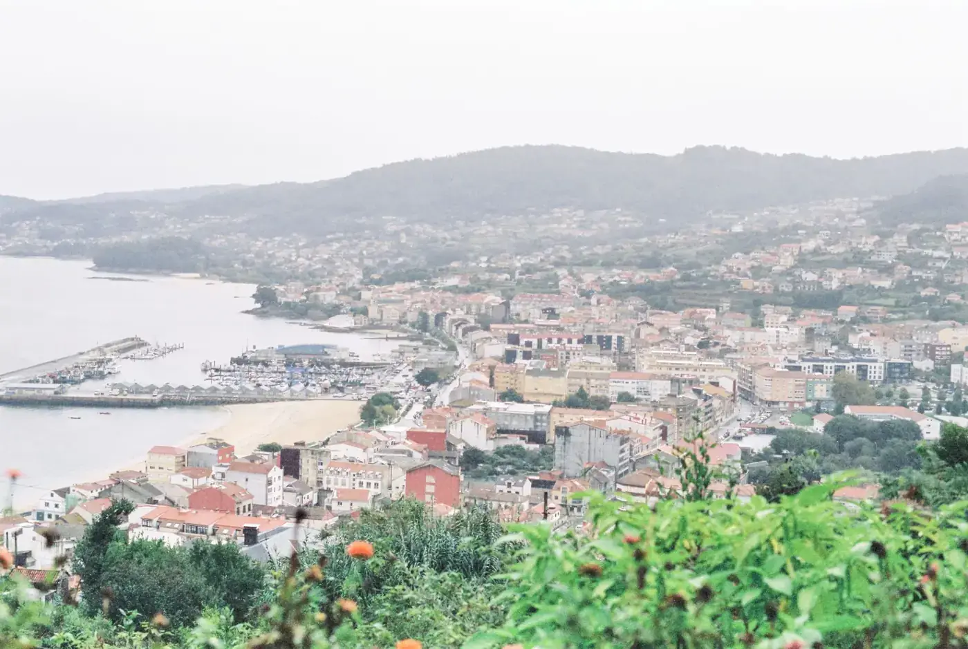 Aerial view of a picturesque coastal city with a harbor, surrounded by natural landscapes.