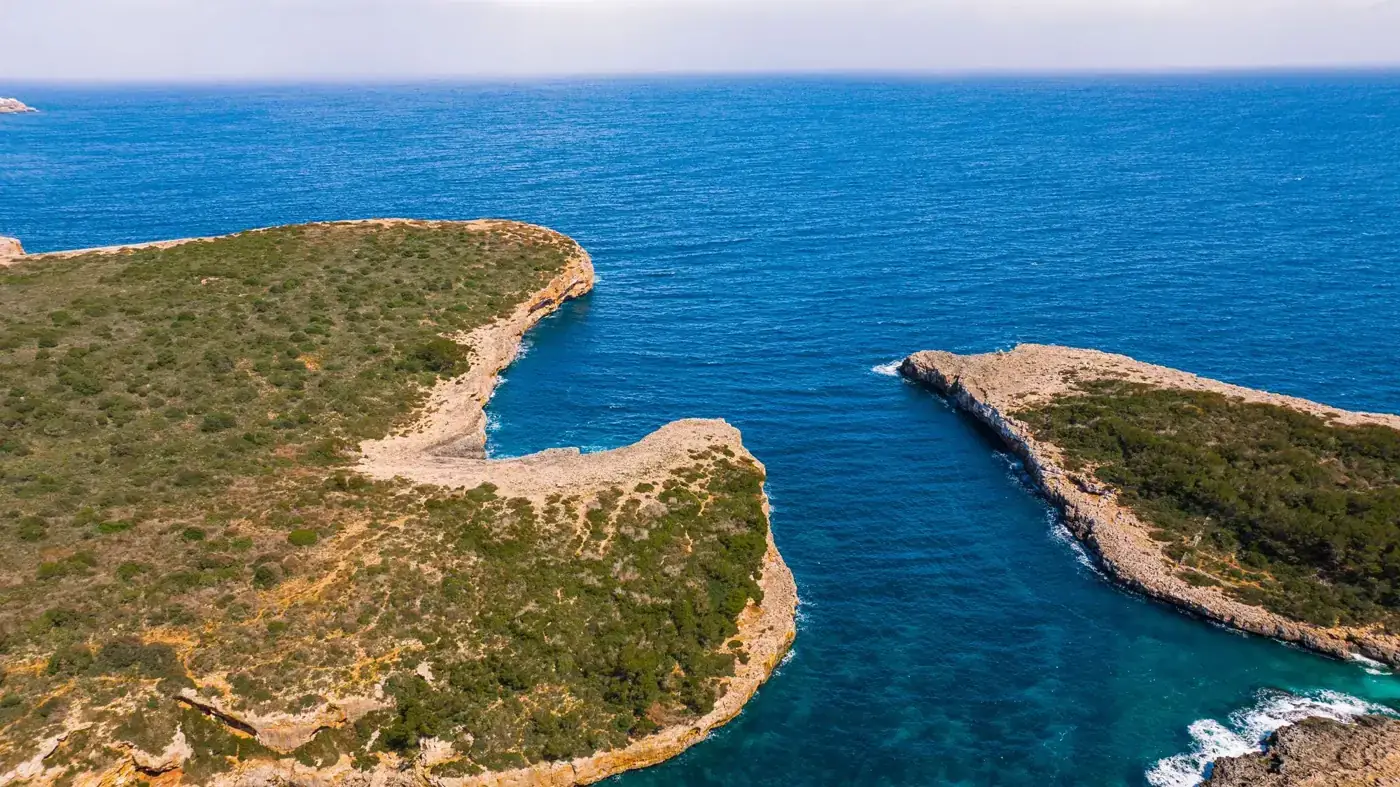 A stunning aerial view of Mallorca's rugged coastline with turquoise waters and lush green cliffs.