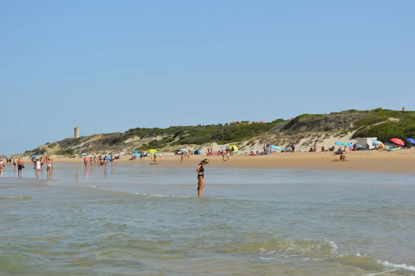 Crowded summer beach in Spain with tourists and clear blue skies.