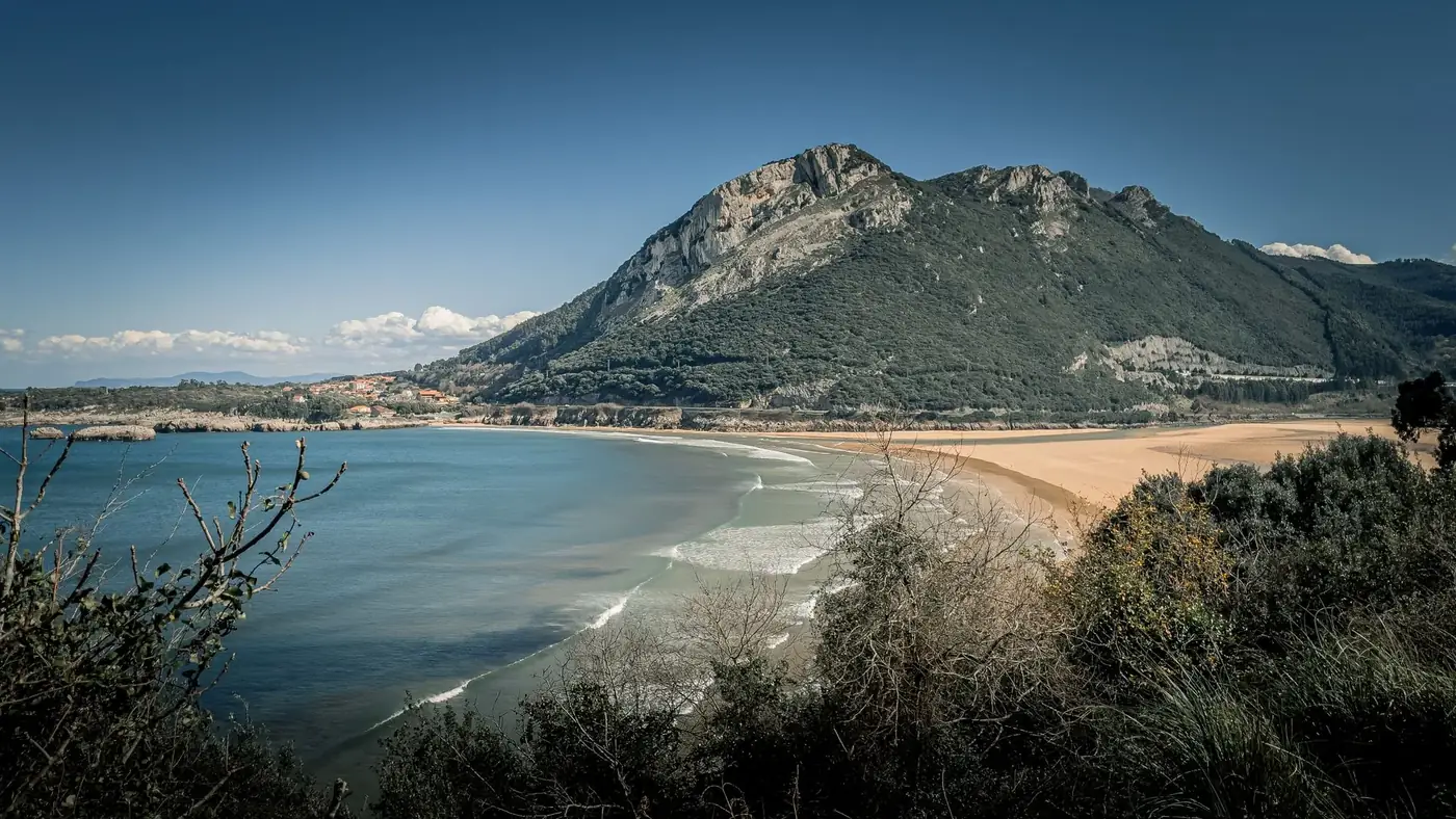 Beautiful coastal view of beach and mountainous landscape in Castro-Urdiales, Spain, under a clear blue sky.