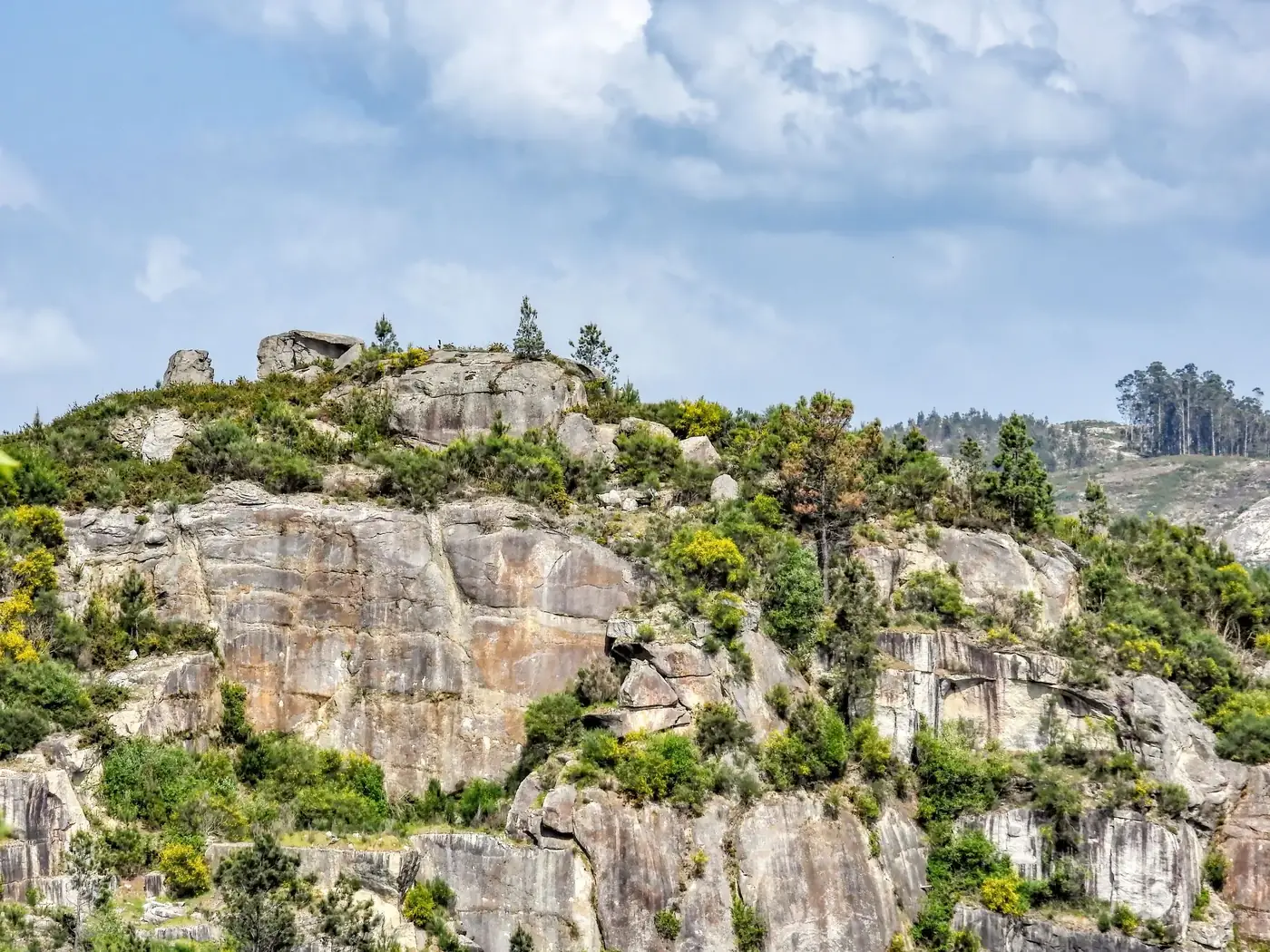 Scenic rocky hillside with lush greenery under a cloudy sky in Galicia, Spain.