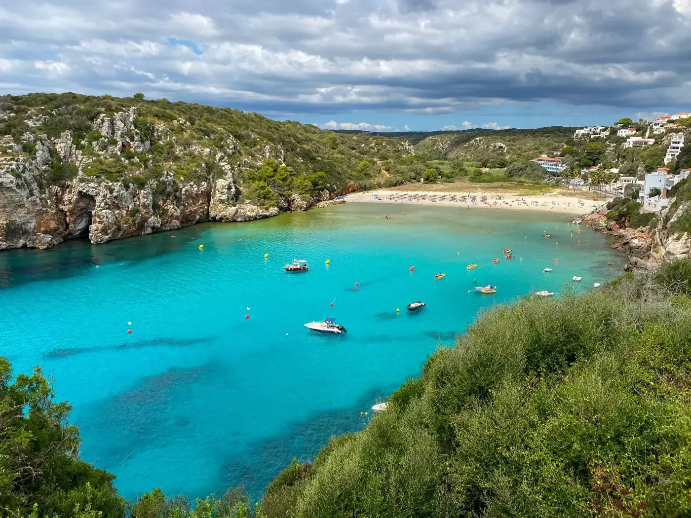 Stunning aerial shot of the vibrant Cala en Porter beach in Menorca, showcasing turquoise waters and rugged cliffs.