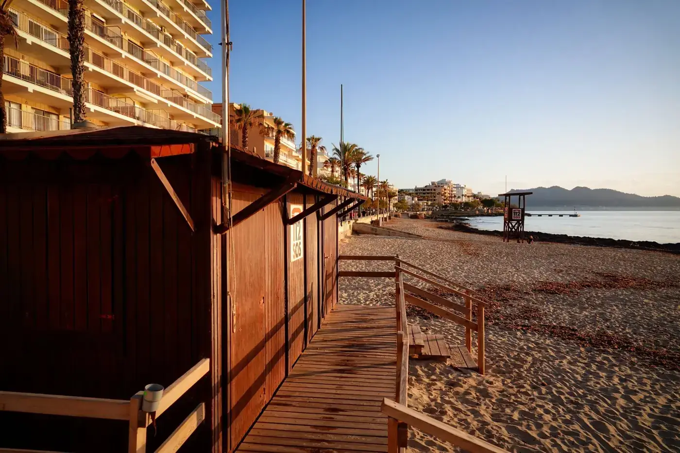 Scenic view of Cala Millor beach with lifeguard hut and palm trees at sunrise, Spain.