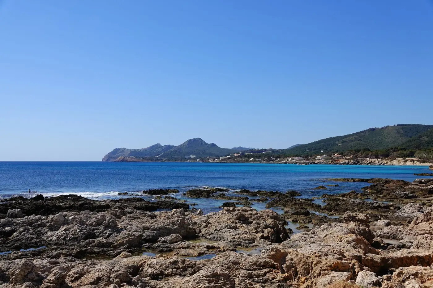 Explore the serene rocky coastline of Cala Rajada, Spain, with clear blue waters and scenic mountains.