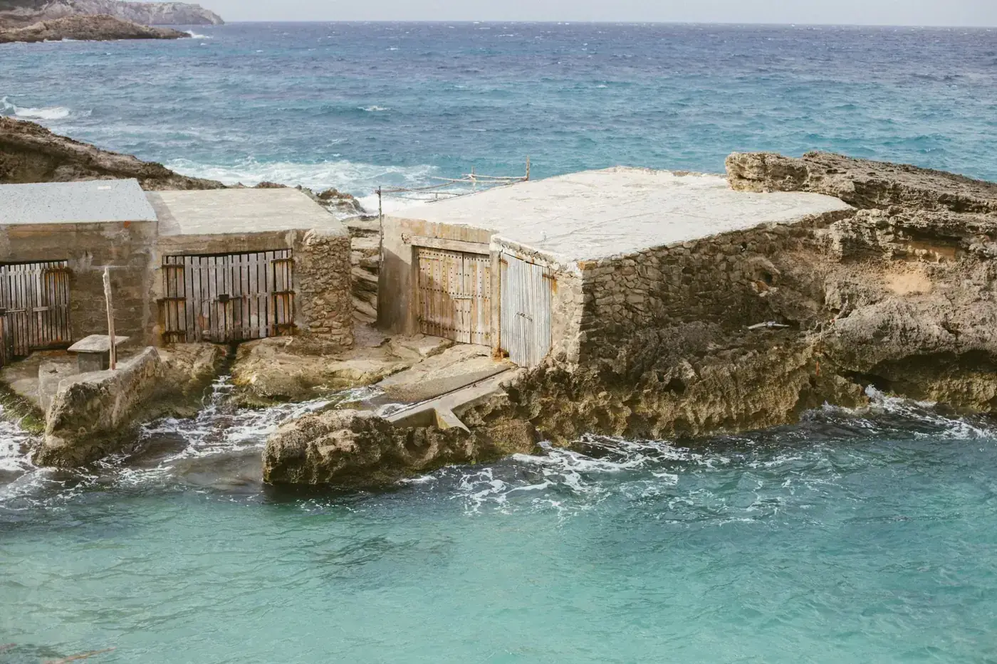 Weathered fishermen's sheds by the azure sea in Ibiza, Spain, showcasing rustic coastal charm.