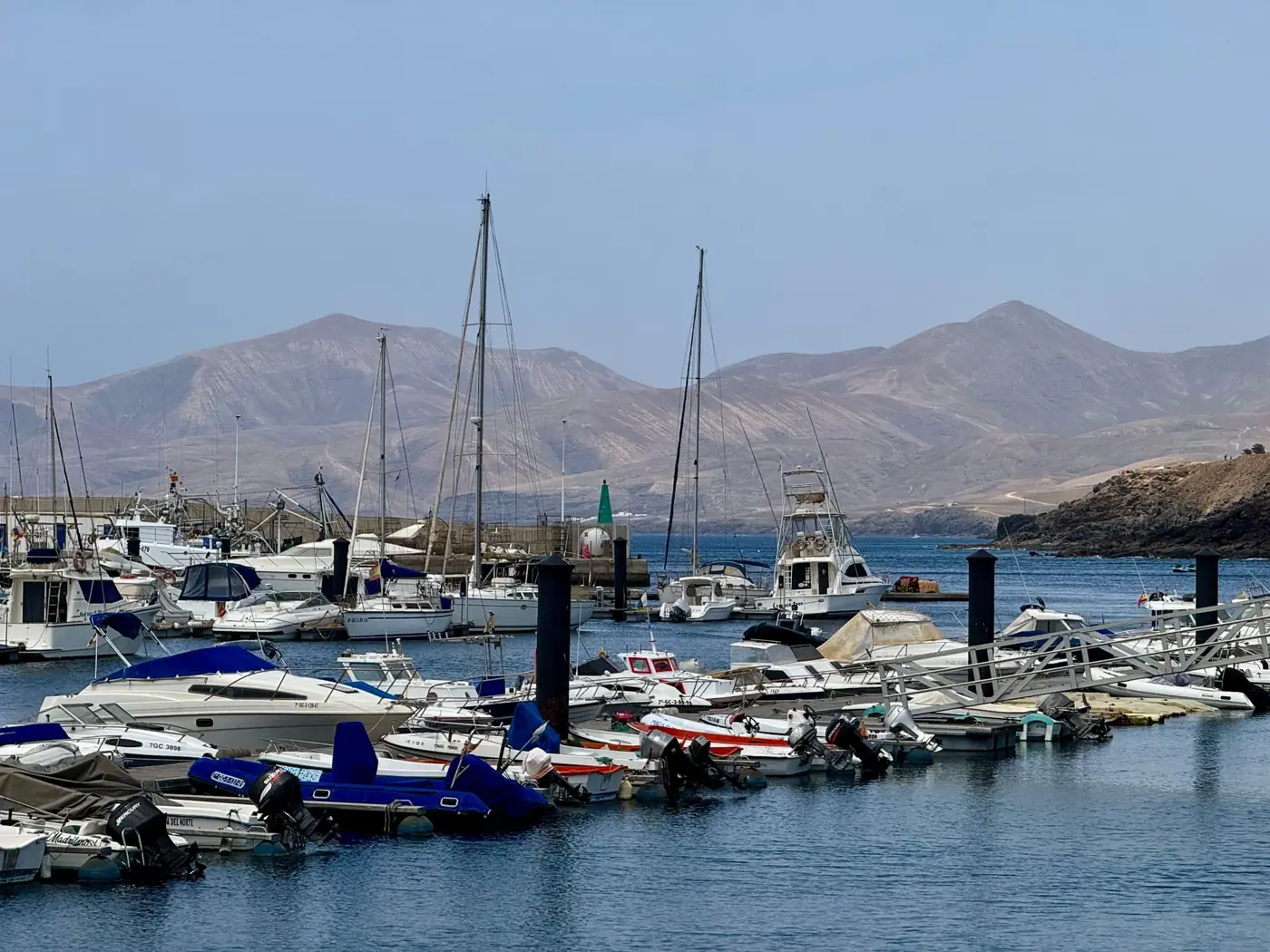 A picturesque harbor scene in Lanzarote, Spain, featuring boats docked against a backdrop of majestic mountains.