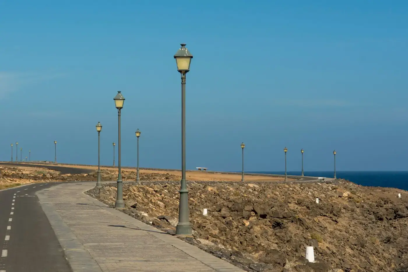 A serene coastal road lined with vintage street lanterns and ocean view.