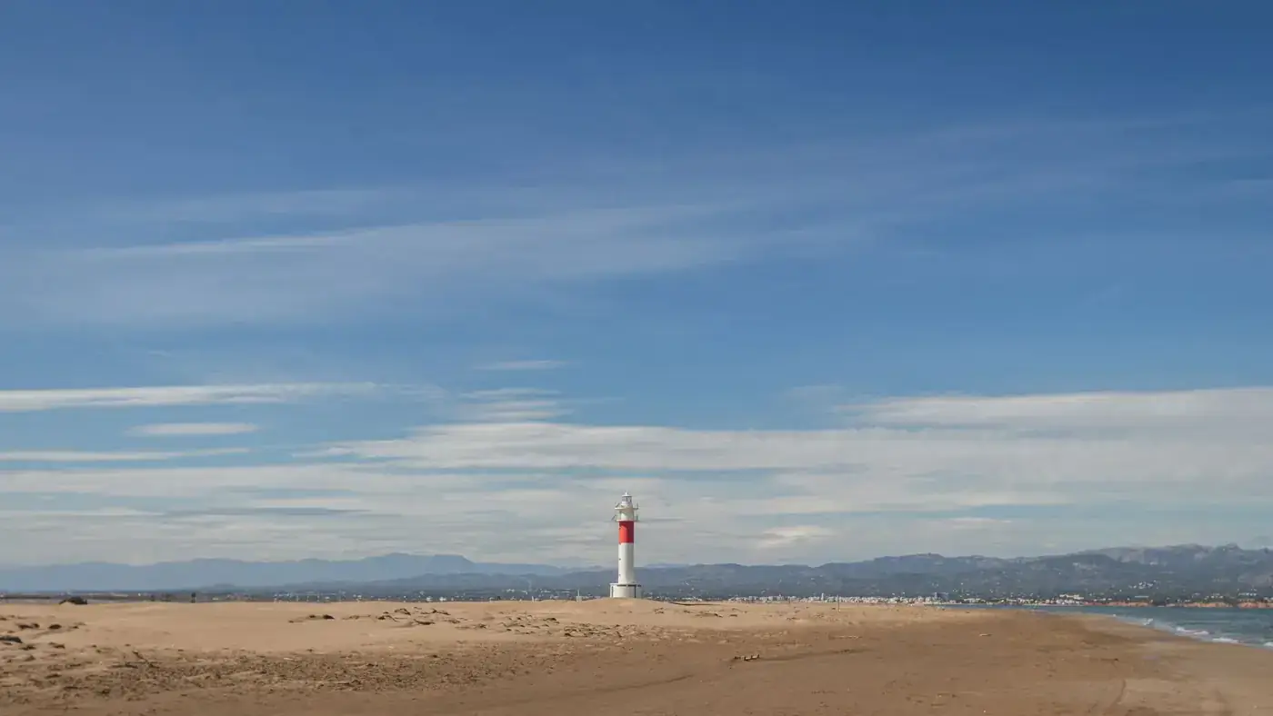A tranquil beach setting featuring a prominent lighthouse under a clear blue sky.