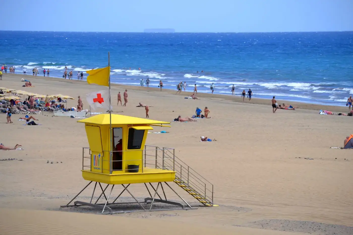Lively summer scene on Maspalomas Beach, Gran Canaria, with a yellow lifeguard tower and beachgoers.
