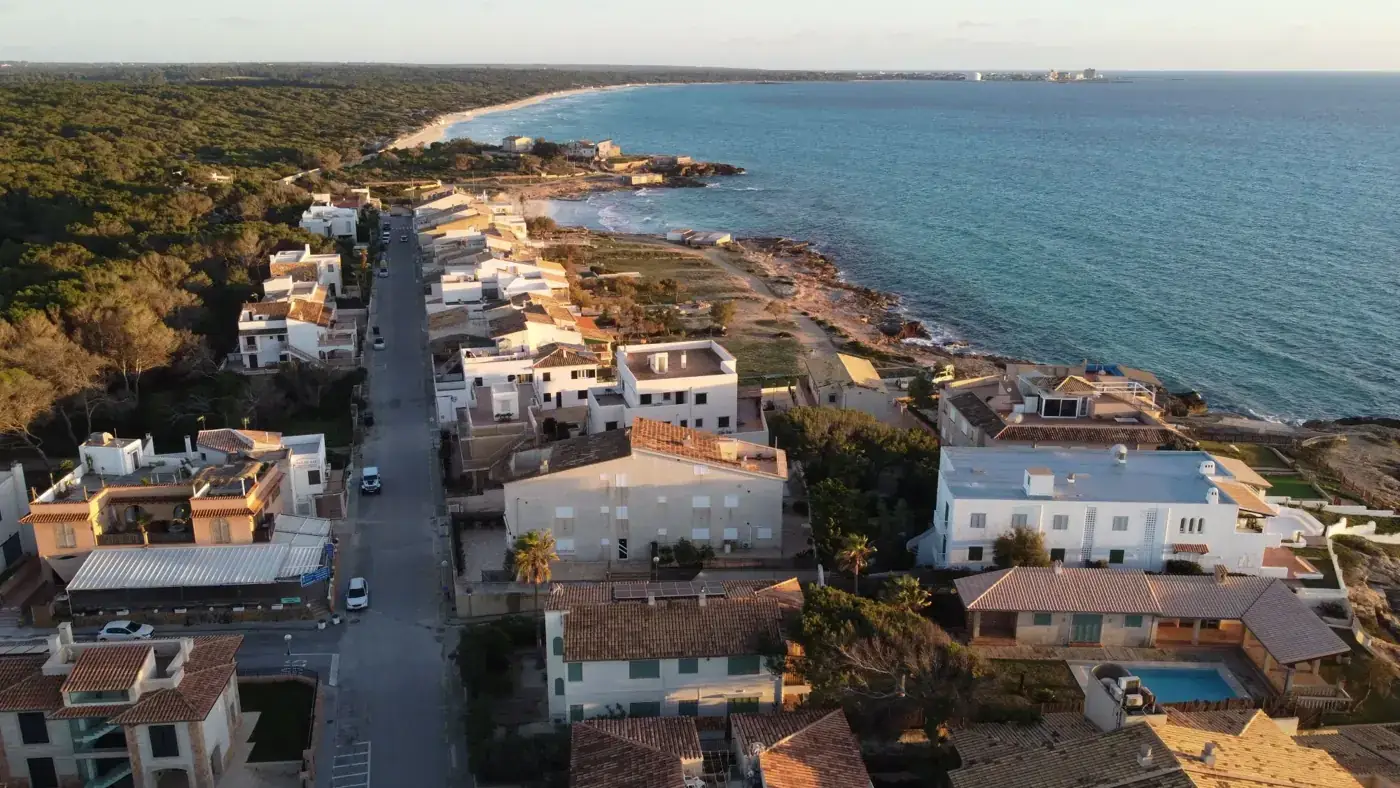 Aerial view of Ses Covetes, Balearic Islands, showcasing coastal homes and serene seascape at sunset.