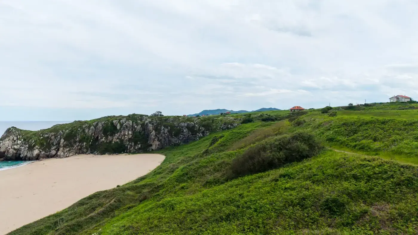 Lush green hills meet a rocky coastline and sandy beach in a tranquil Spanish landscape.