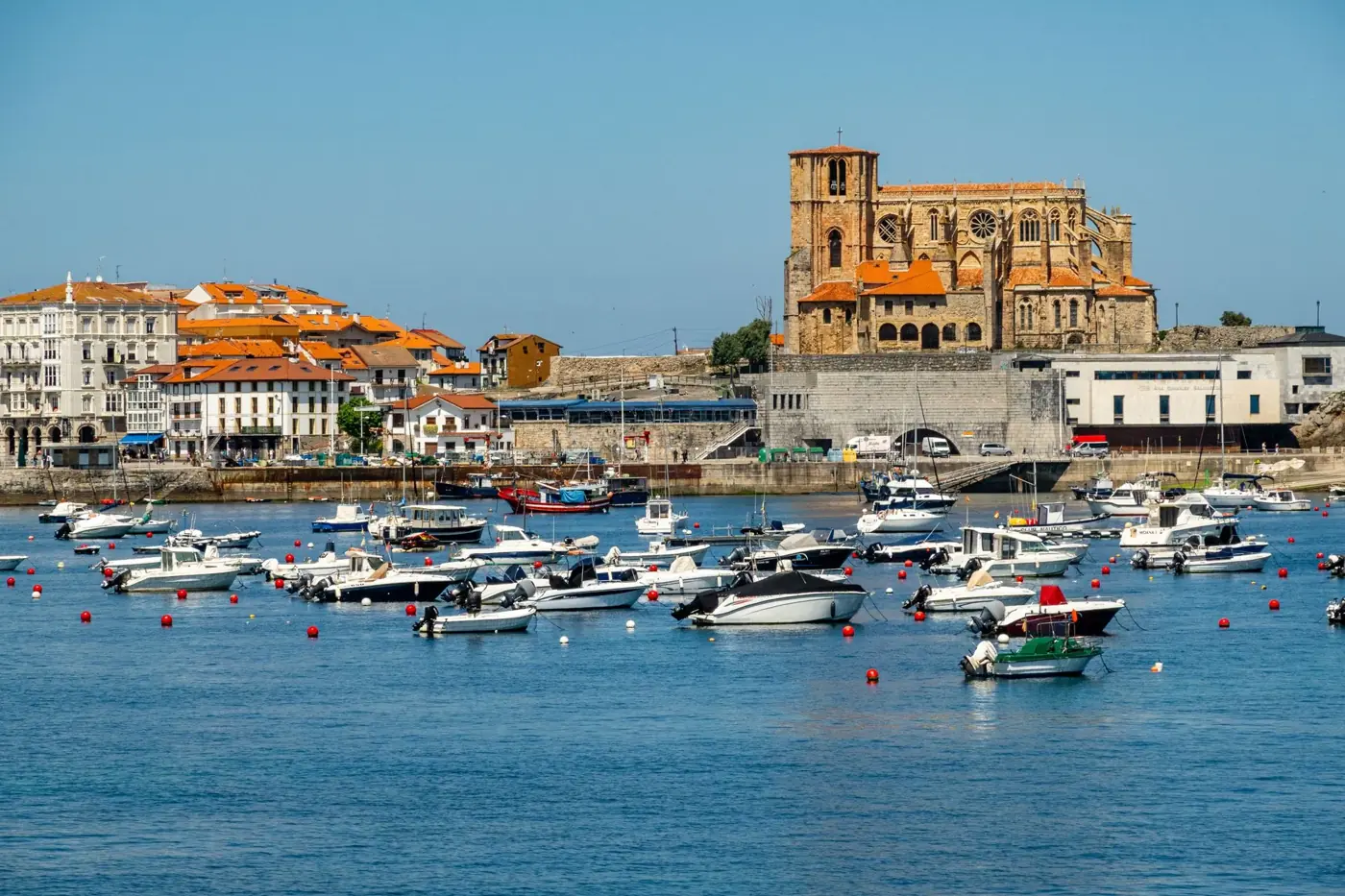 Scenic view of Castro Urdiales harbor with numerous boats and Santa María de la Asunción Church.