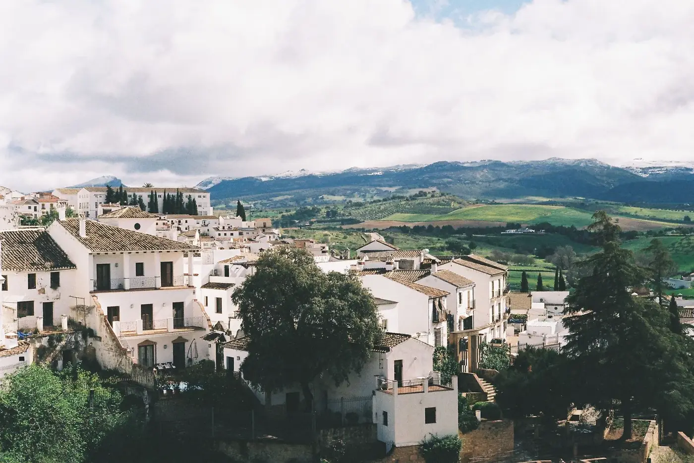 A picturesque view of a Spanish town with white houses, surrounded by green hills and distant mountains.
