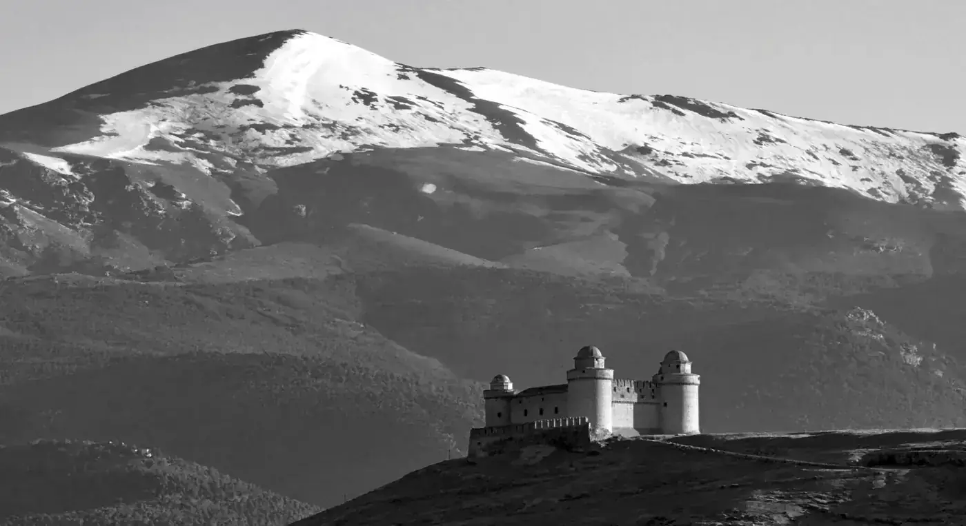 Black and white view of Castillo de La Calahorra set before snowcapped mountains in Spain.
