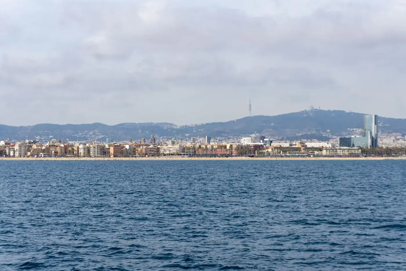 Stunning panoramic view of Barcelona coastline with urban skyline and distant hills under a cloudy sky.