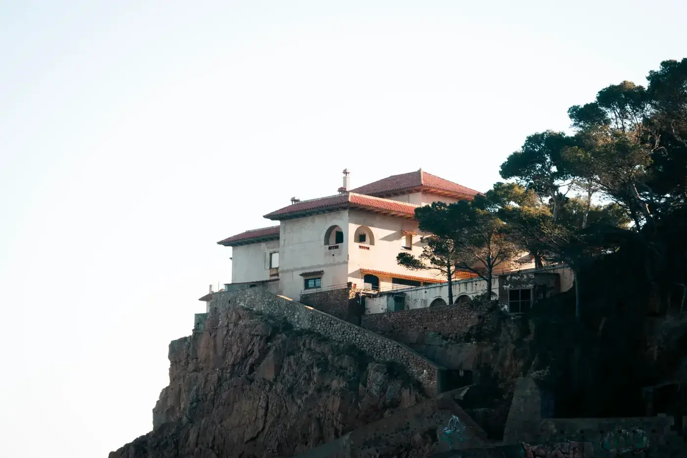 Elegant villa perched on a cliff in Costa Brava, framed by trees against a clear sky.