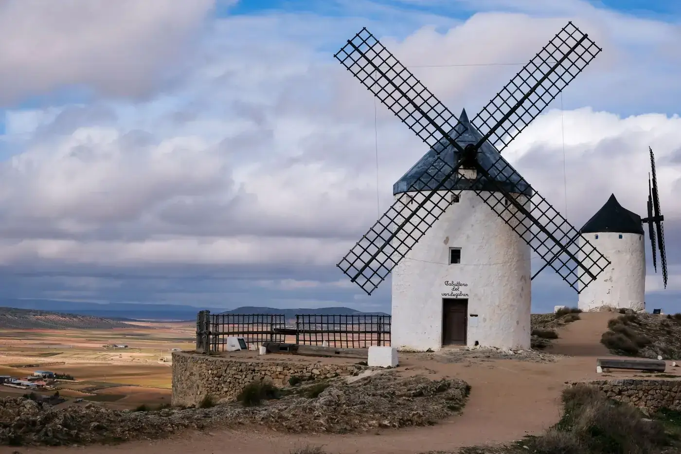 Scenic view of historic windmills in Consuegra, Spain against a cloudy sky.