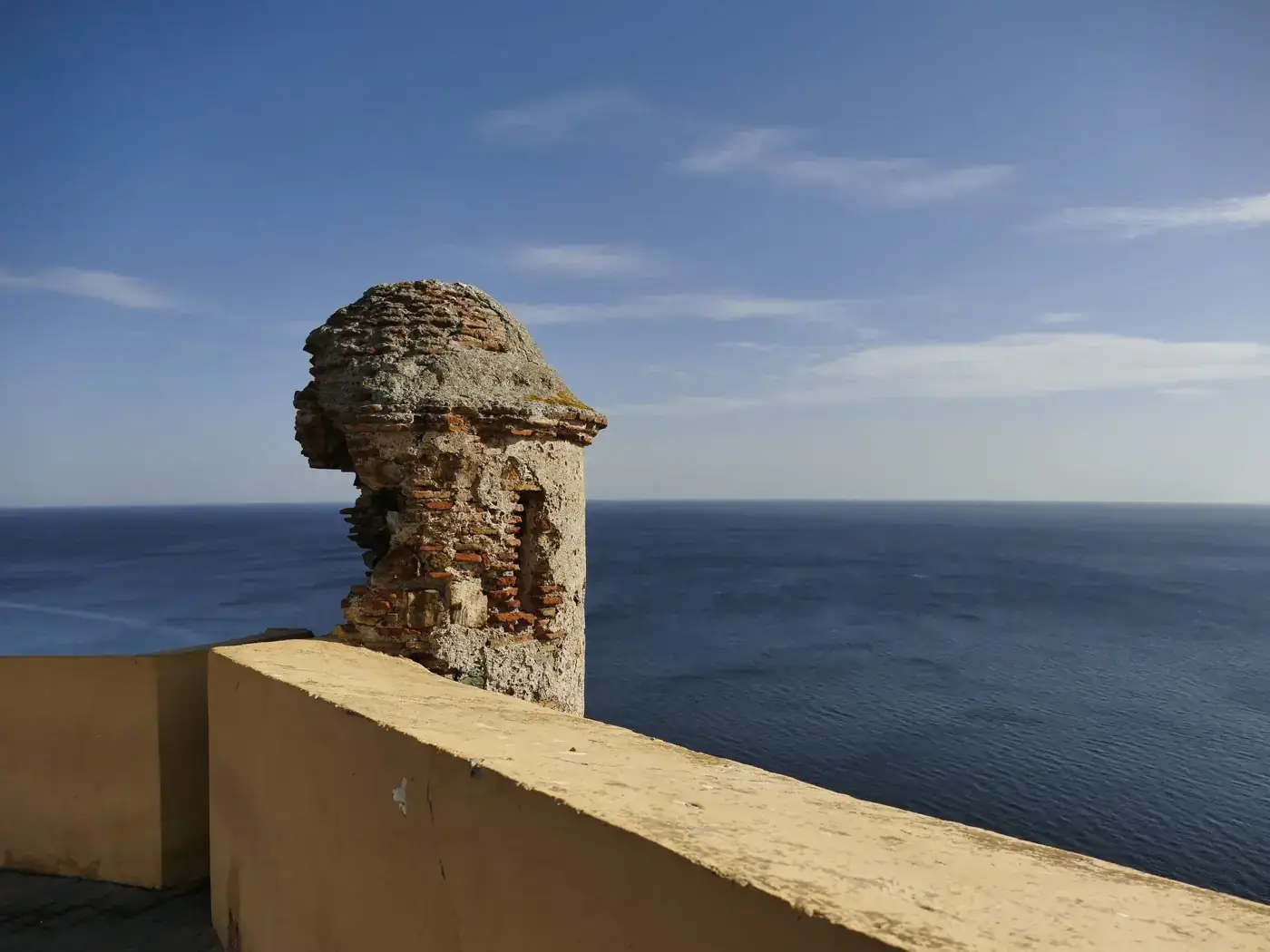 Ancient fortification wall in Ceuta overlooking the vast blue sea on a clear summer day.