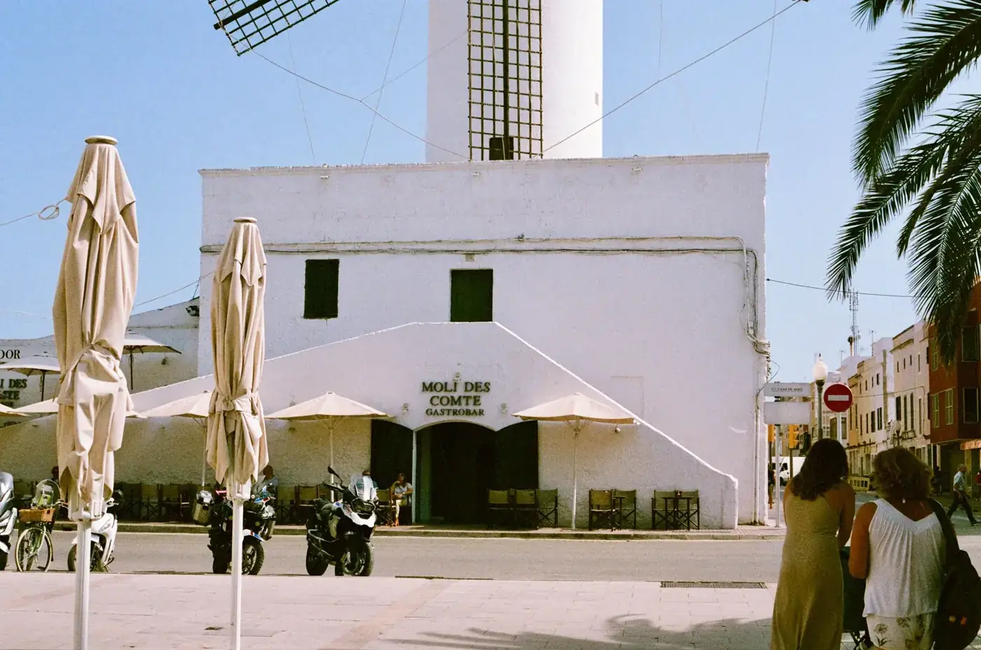 Charming white-washed Moli des Comte restaurant in Ciutadella with umbrellas and palm trees.
