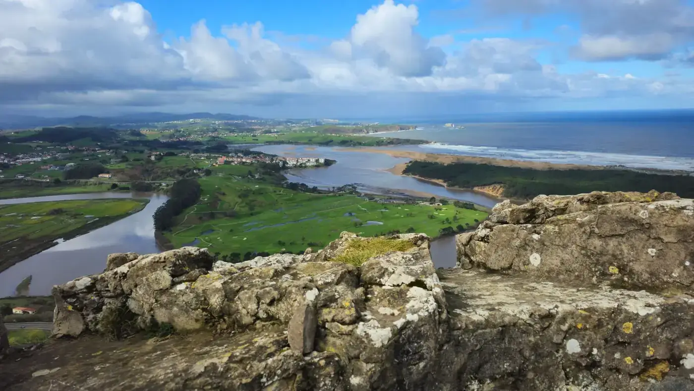 Breathtaking view of Cantabria's coastline, lush countryside, and rocky foreground under a vibrant sky.