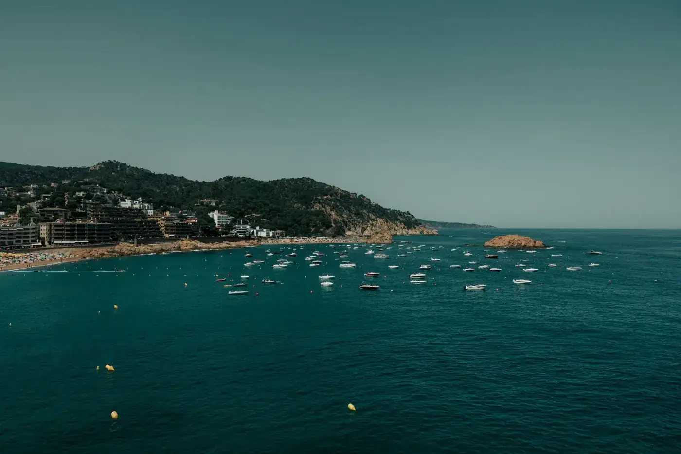 A picturesque view of Tossa de Mar's coastline featuring boats and lush landscapes under a clear sky.