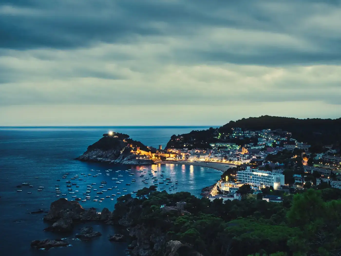 Scenic night view of Tamariu, Spain with illuminated waterfront and boats in the bay.