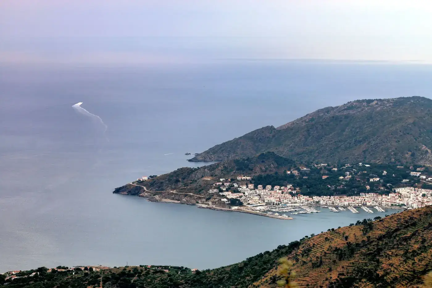 A stunning aerial view of a coastal town in Spain, showcasing its harbor and surrounding mountains.