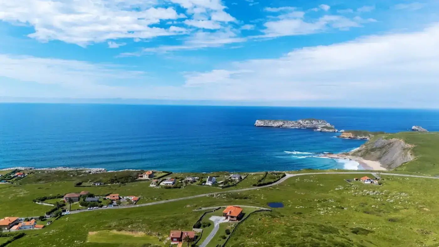 Stunning aerial shot of Costa Quebrada coastline with lush green fields meeting the blue sea under a clear sky.