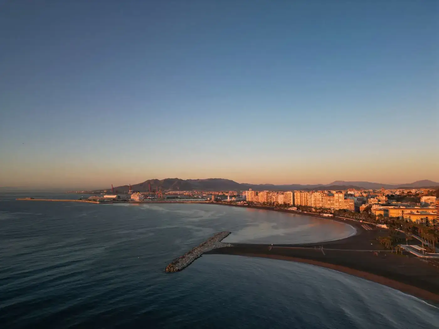 Aerial view of Málaga's coastline with sunlit buildings at sunset, showcasing the beautiful bay.