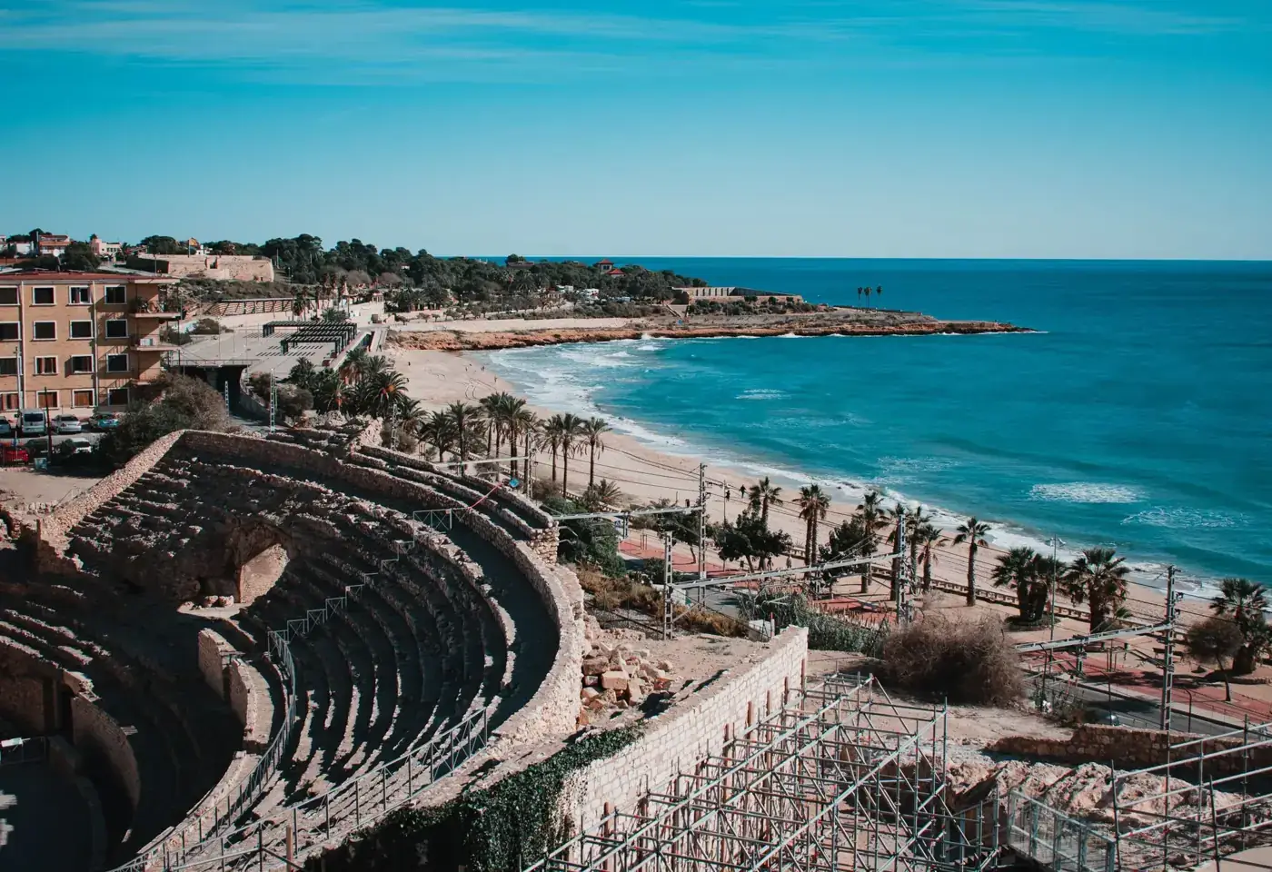 Stunning aerial view of Tarragona amphitheater with coastal shoreline, palm trees, and clear blue sea in Spain.