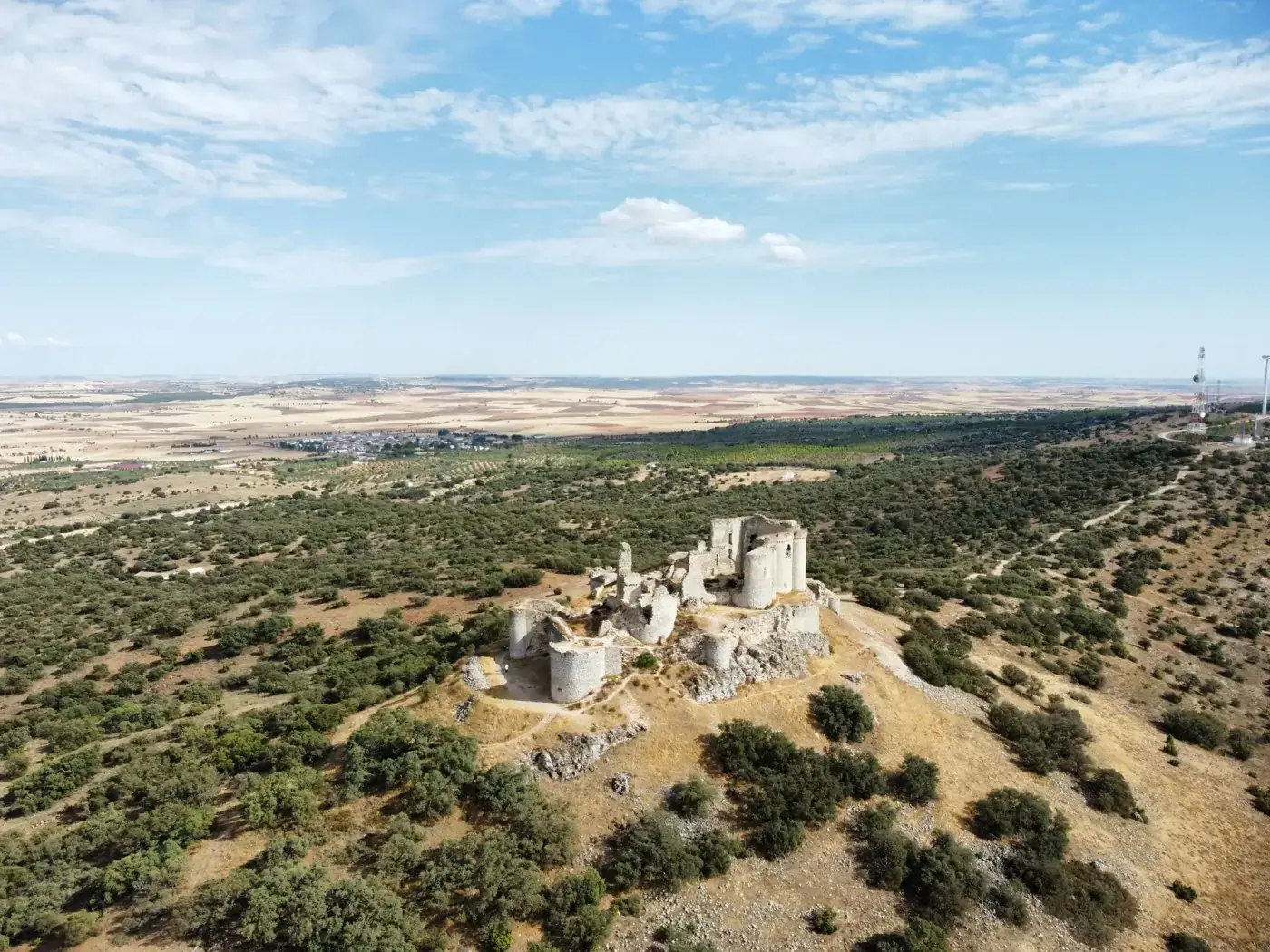 A drone captures the scenic ruins of a castle amidst the natural landscape of La Mancha, Spain.