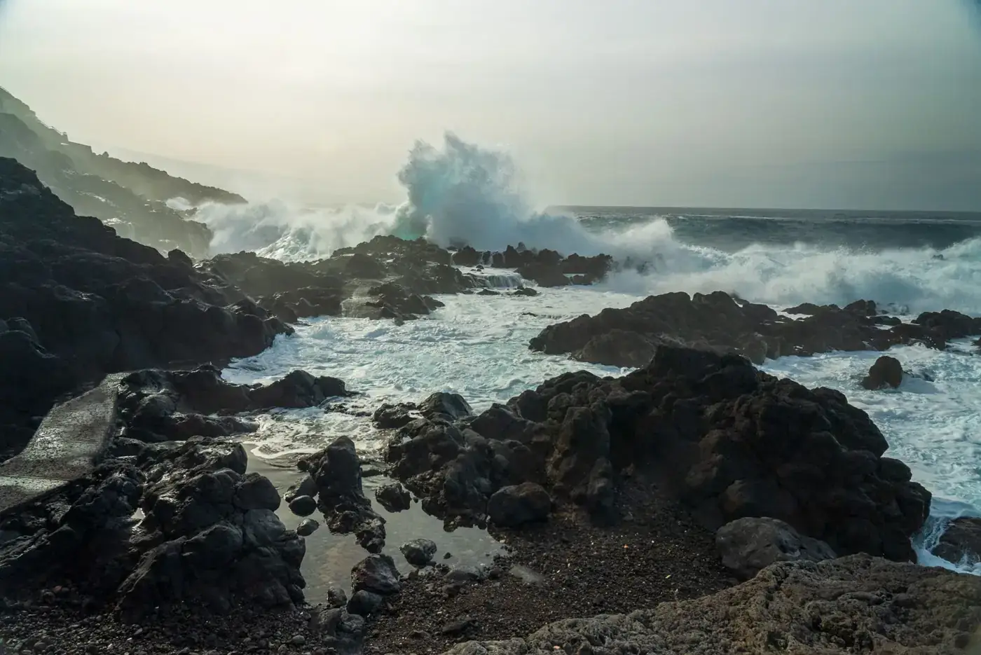 Powerful waves crashing on a rocky shoreline in El Sauzal, Spain, during a cloudy day.