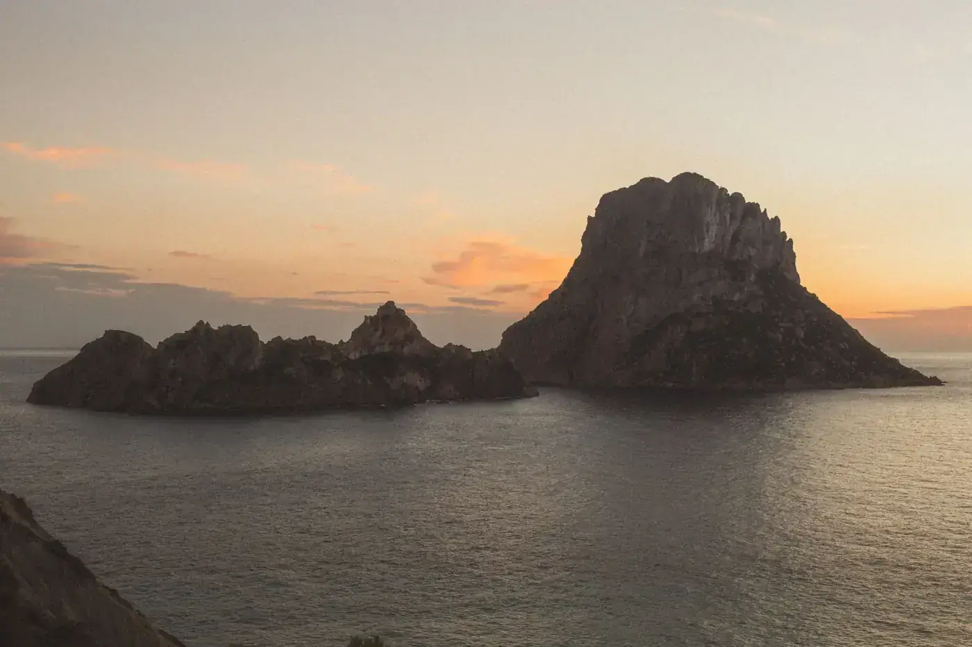 Stunning sunset view of the Es Vedrà island in Ibiza, Spain with calm waters and vibrant skies.