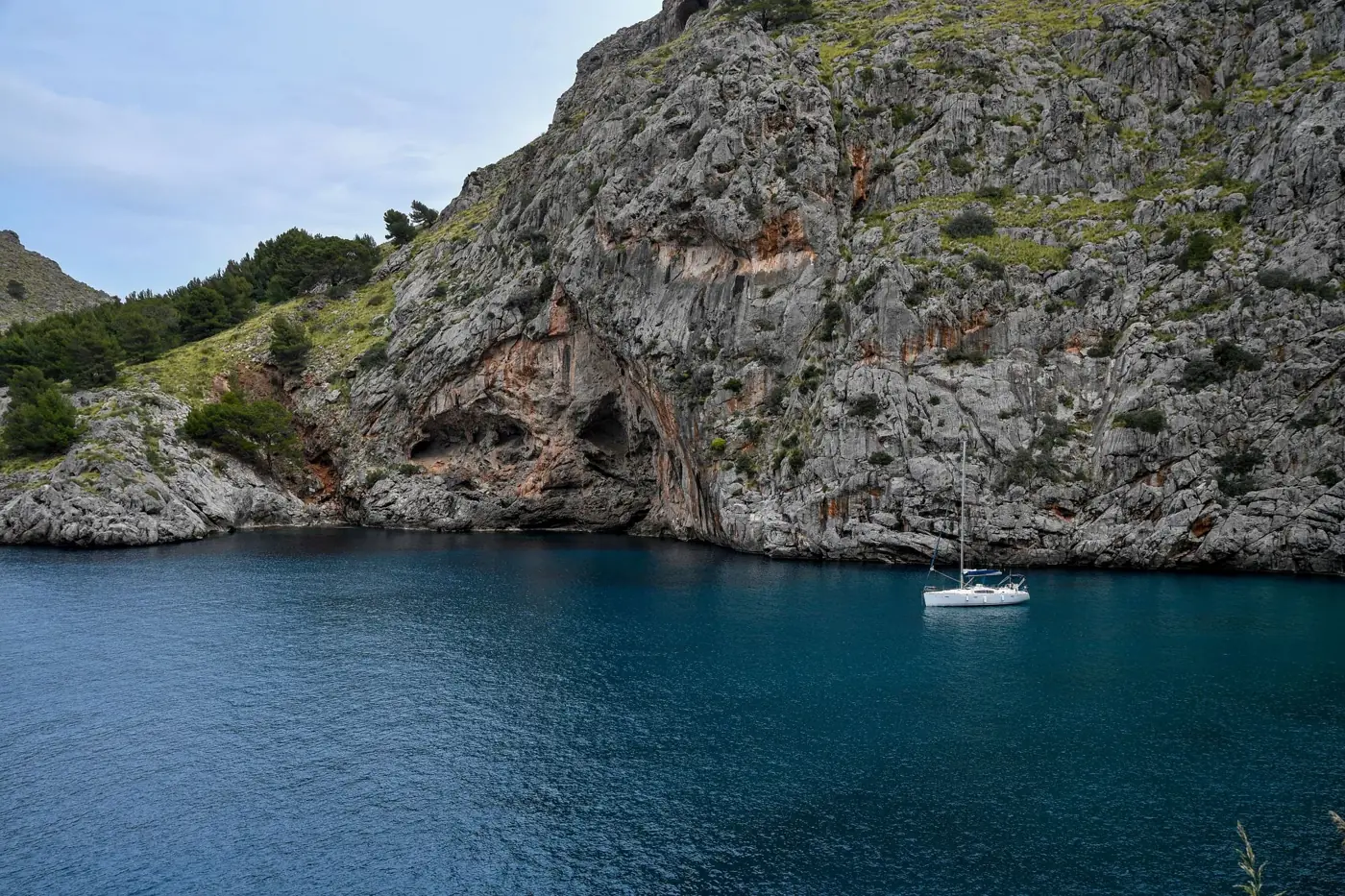 A tranquil scene with a sailboat anchored in a turquoise cove surrounded by rocky cliffs.