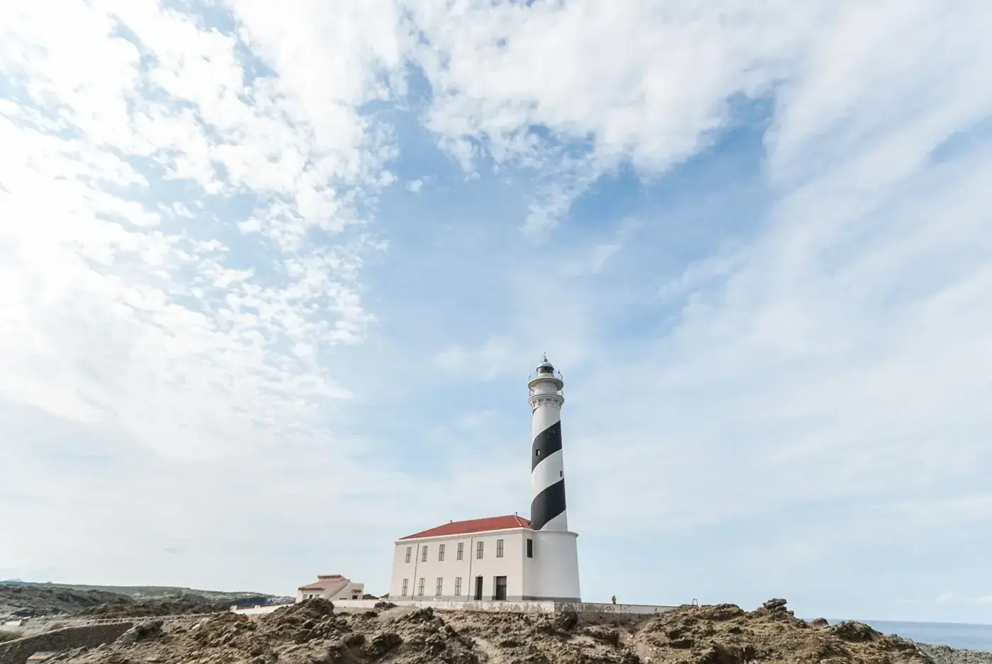 Idyllic lighthouse on rocky Spanish coast under a bright, cloudy sky.
