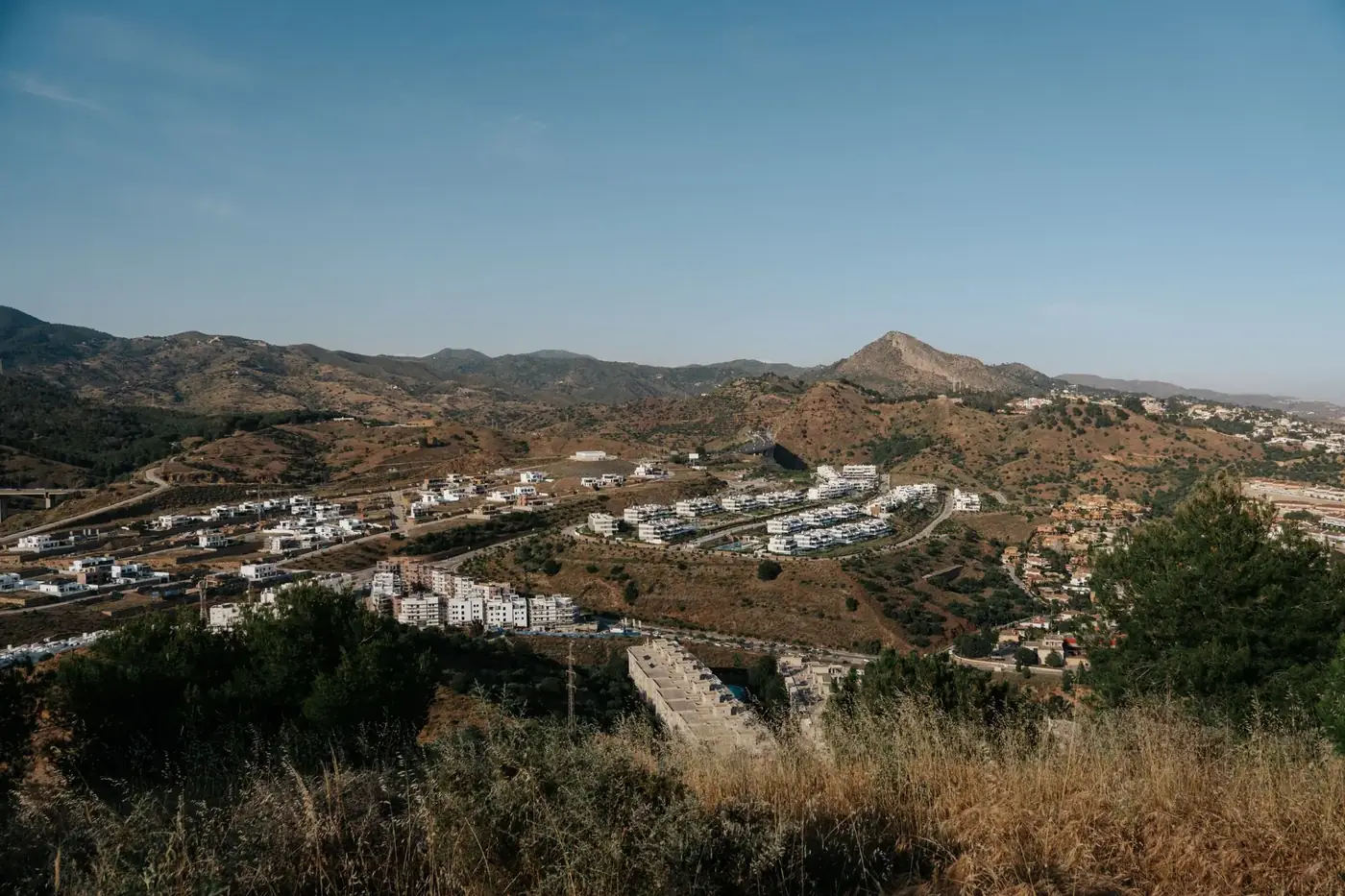 Capture of Málaga, Spain's scenic landscape featuring white buildings nestled in rolling hills under a clear summer sky.