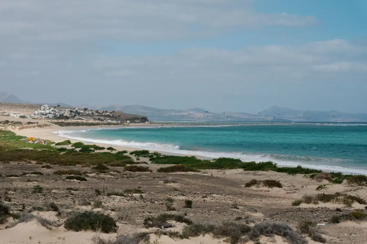 Beautiful landscape of a coastal area with turquoise ocean, sandy beach, and distant mountains.