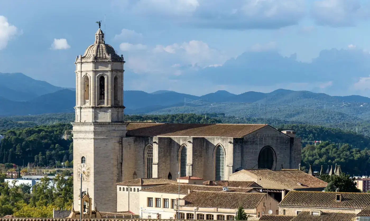 A beautiful view of Girona Cathedral against a mountain backdrop and clear blue skies.