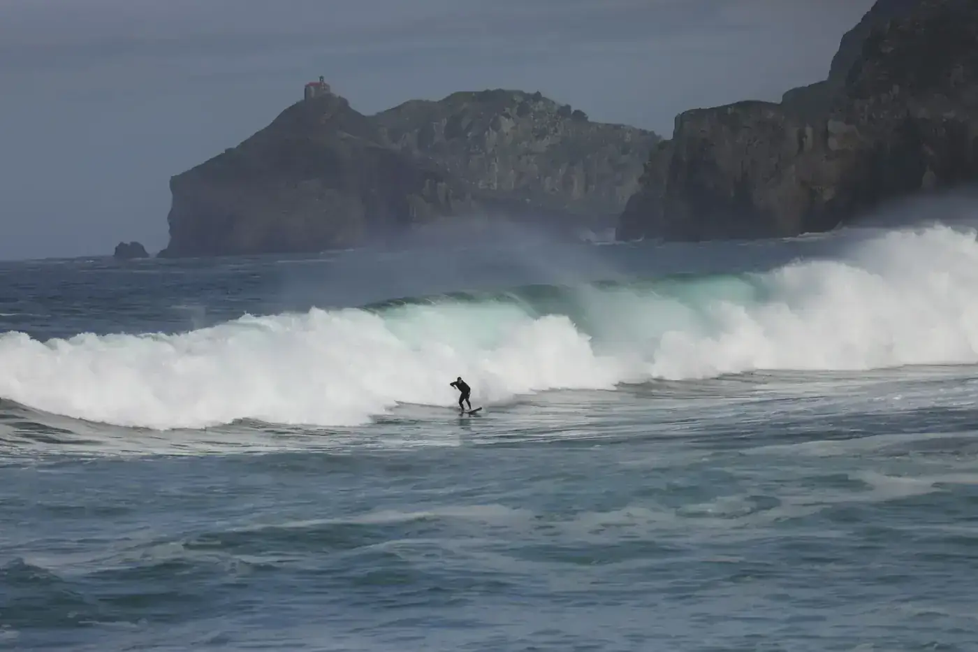A lone surfer rides a wave against stunning coastal cliffs at Bakio Beach, Basque Country.