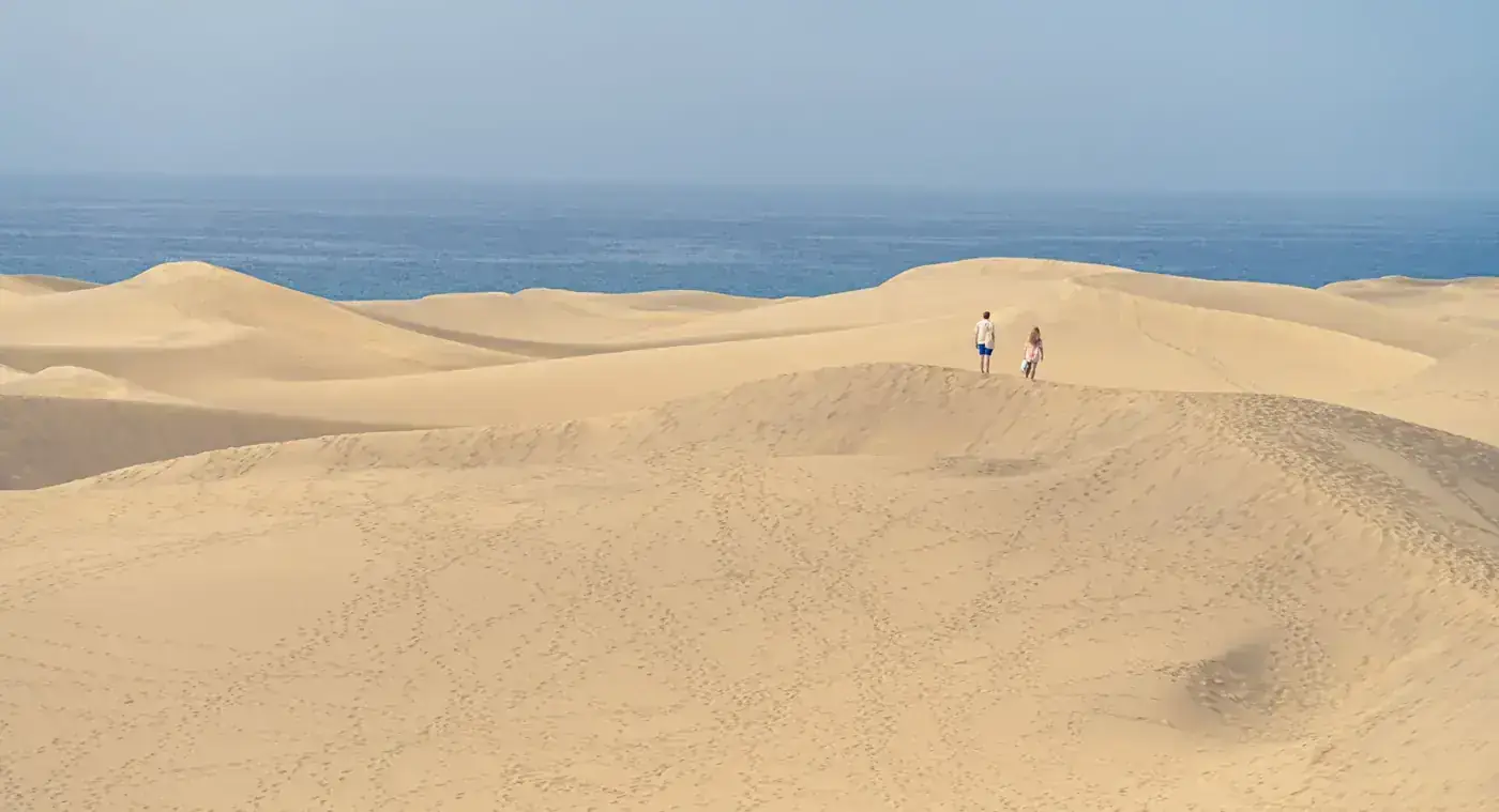 Peaceful dunes of Maspalomas in Spain with ocean views and two people exploring.