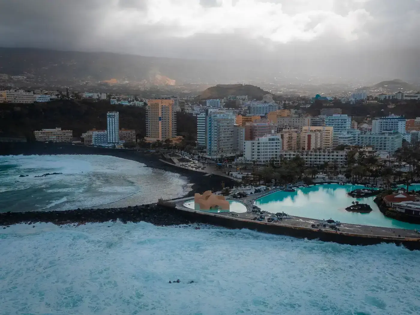 Dramatic aerial view of Puerto de la Cruz, Tenerife with stormy skies and ocean waves.